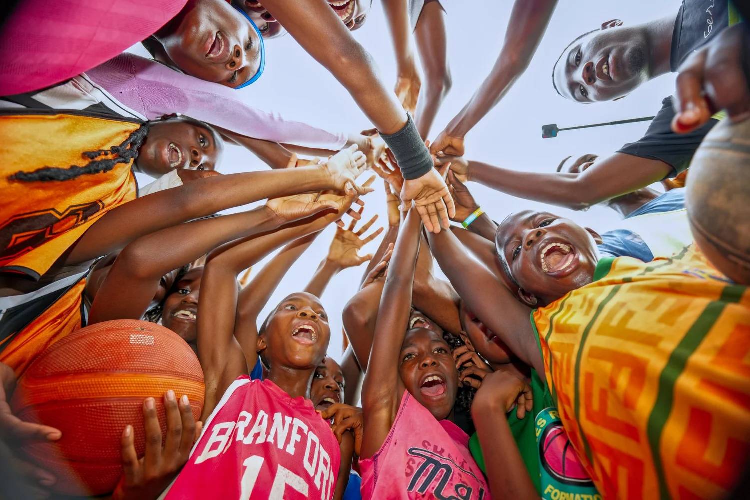A group of young athletes with their hands joined in a huddle around a basketball